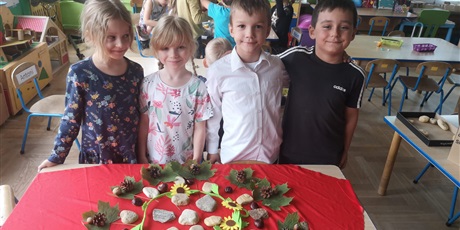 Powiększ grafikę: Czwórka dzieci prezentuje stworzoną przez siebie mandalę z kamieni, liści, kasztanów i szyszek.