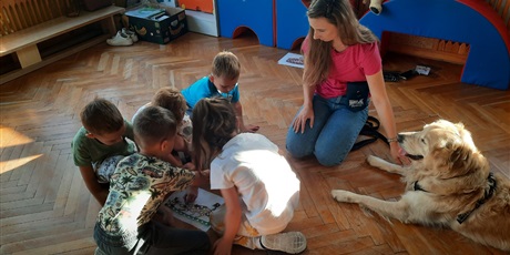 Powiększ grafikę: Terapeuta z psem oraz grupka dzieci wykonuje zadanie na podłodze.