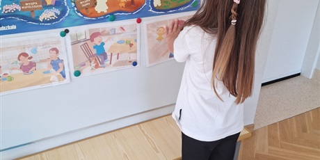 Powiększ grafikę: Dziewczynka przypina do tablicy obrazki.