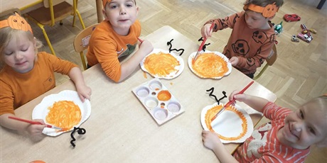 Powiększ grafikę: Czwórka dzieci maluje pomarańczową farbą papierowe talerzyki