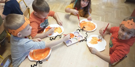Powiększ grafikę: Czworo dzieci maluje pomarańczową farbą papierowe talerzyki