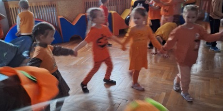 Powiększ grafikę: Dzieci ubrane na pomarańczowo tańczą w kole.