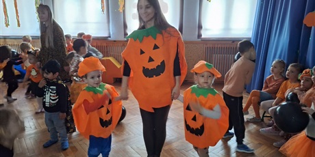 Powiększ grafikę: Nauczycielka z dwójka dzieci w przebraniach dyni, na drupim planie bawiące się dzieci.