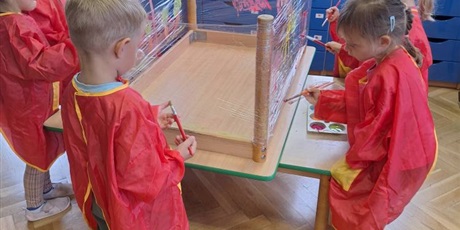 Powiększ grafikę: eDzieci malują farbami po foli spożywczej przyczpionej do nóg stołu odwróconego do góry nogami.