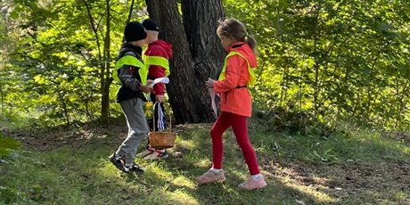 Powiększ grafikę: Trójka dzieci zbiera kasztany do koszyka.