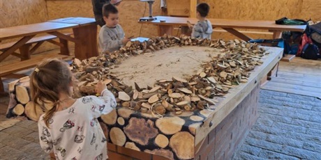 Powiększ grafikę: Dwoje dzieci wybiera plastry drewna znajdujace się na wielkim stole. 