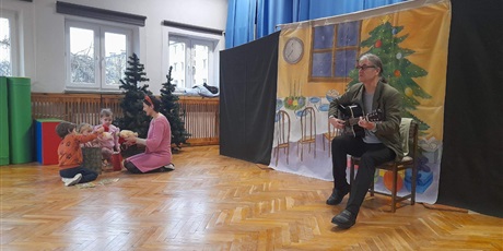 Powiększ grafikę: Jeden z aktorów gra na gitarze, a drugi wspólnie z dziećmi oglądają prezenty.