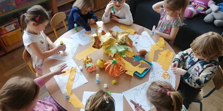 Powiększ grafikę: Grupka dzieci wykleja obrazek dyni pomarańczowym papierem.