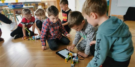 Powiększ grafikę: Dzieci z grupy "Żabek" patrzą w tablet na instrukcję budowy robota z klocków lego.